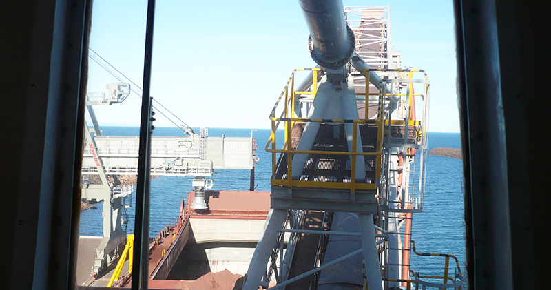 Siwertell ship loader seen from terminal building window above, iron ore in ship hold being loaded