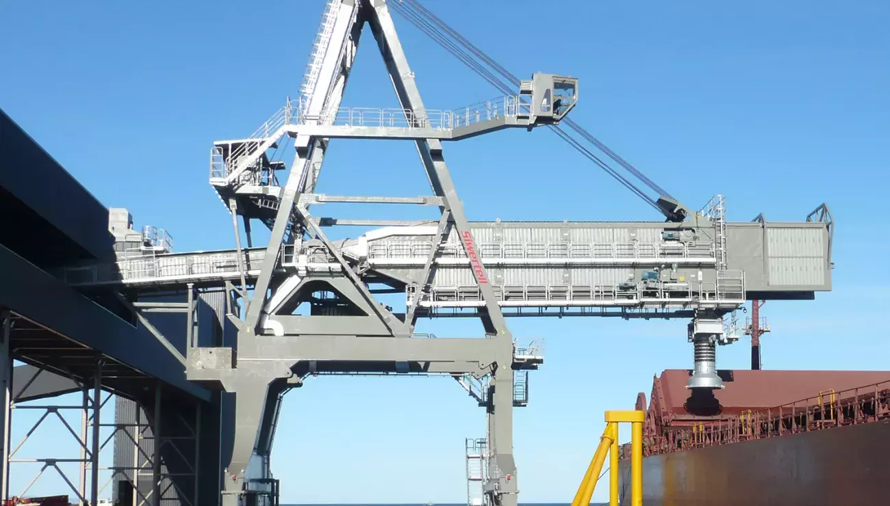 Siwertell ship loader on jetty loading iron ore into ship, blue sky