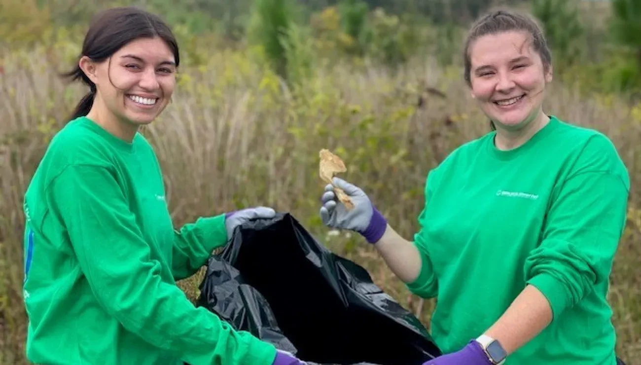 Two women in green shirts holding plastic bag