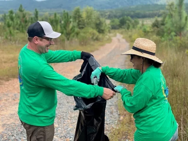 Two people in green shirts putting trash in plastic sack