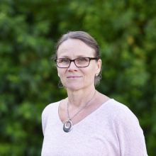 Woman with glasses in pink shirt standing in front of green bushes
