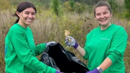 Two women in green shirts holding plastic bag