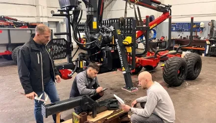 Forest crane and trailer with three men discussing spareparts