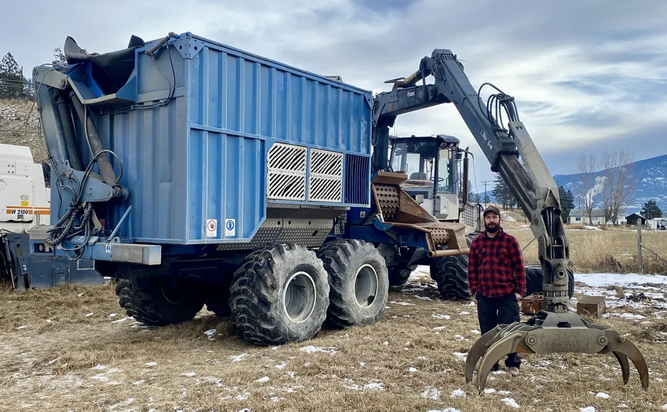 a man standing beside a blue mobile chipper machine
